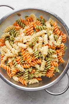 a bowl filled with pasta and vegetables on top of a white counter next to a metal strainer