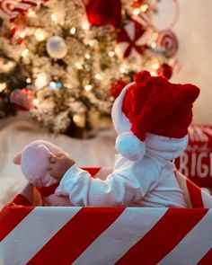 a baby is sitting in a red and white striped box with a christmas tree behind it