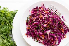 a white plate topped with red cabbage and broccoli next to a fork on top of a table