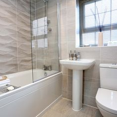 a white toilet sitting next to a bath tub under a window near a sink with a faucet