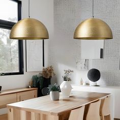 two lamps hanging over a wooden table in a room with white walls and wood furniture