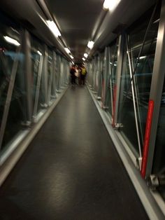 people walking down a long hallway with glass walls and red railings on both sides