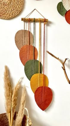 a wall hanging made out of different colored circles on a white wall next to dried plants