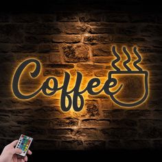 a person holding a cell phone in front of a brick wall with the word coffee on it