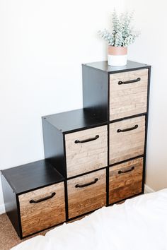 three drawers are stacked on top of each other in front of a white wall with a potted plant