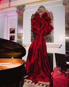 a large red dress sitting on top of a table in front of a grand piano