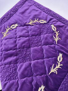 a close up of a purple quilt with gold thread work on it and an applique