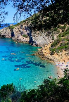 the beach is surrounded by trees and blue water, with people swimming in the water