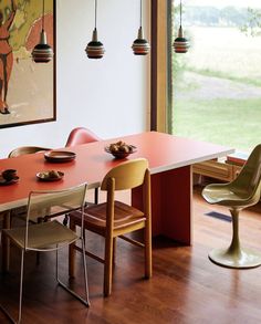 a dining room table and chairs in front of a large window with a painting on the wall