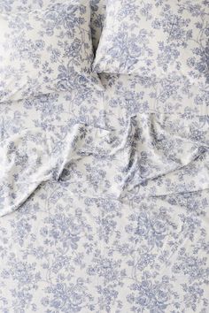 an unmade bed with blue and white flowers on it