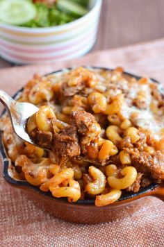 a spoon full of macaroni and cheese with meat in it on a table