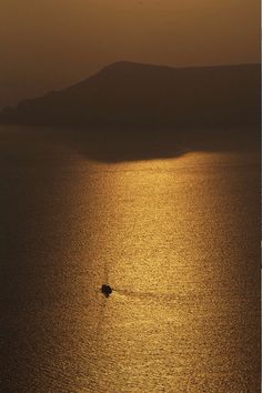 a small boat in the middle of an open body of water at sunset with mountains in the distance