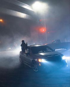 a car driving down a street with fog coming from the hood and headlights on it