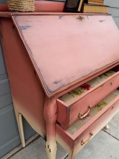 an old pink desk with drawers and books on it's top, in front of a garage door