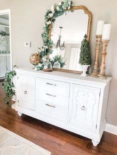 a white dresser topped with a mirror next to a candle holder and vase filled with flowers