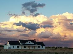 a large white house sitting in the middle of a field under a cloudy blue sky