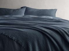 an unmade bed with blue sheets and pillows on top of it, in front of a white wall