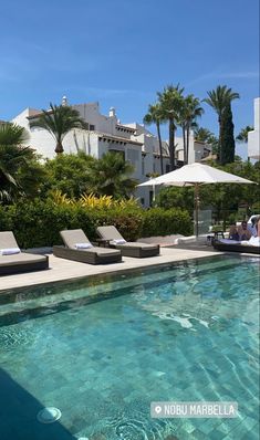 an outdoor swimming pool with lounge chairs and umbrellas next to the side of it