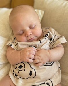 a baby laying on top of a couch with its eyes closed and hands tucked under his chest