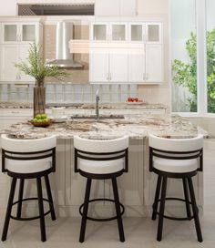 three stools sit at the center of a kitchen island with marble countertops and white cabinets