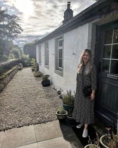 a woman standing in front of a house next to some potted plants and trees