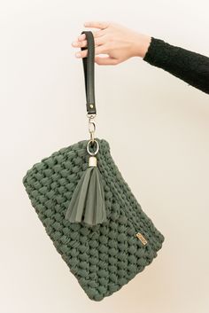 a hand holding a green crocheted bag with tassels on the handle