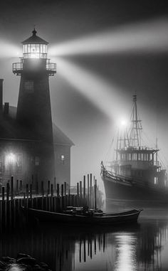 two boats in the water near a light house and pier at night with fog on the ground