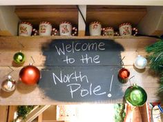 a sign that says welcome to the north pole with ornaments hanging from it's sides