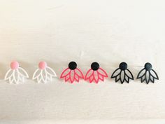 three pairs of earrings with black, pink, and white leaves on them sitting next to each other