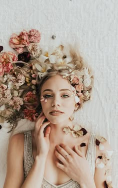 a woman laying on top of a bed with flowers all over her head and hands under her chin