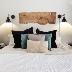 a bed with two lamps on each side and pillows on the bottom, in front of a wooden headboard