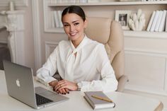 a woman sitting at a desk in front of a laptop computer smiling for the camera