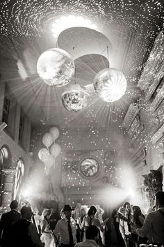 black and white photograph of people dancing in a hall with disco balls hanging from the ceiling