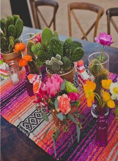 flowers and cactuses are arranged on a colorful table runner at the end of a dining room table