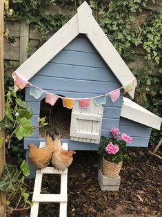 two chickens in a blue and white chicken house with flowers on the side, next to a ladder