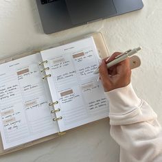 a person writing on a planner next to a laptop