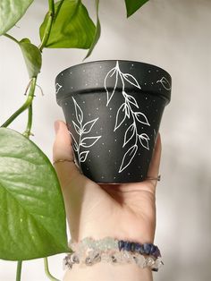 a hand holding a black pot with white leaves on it