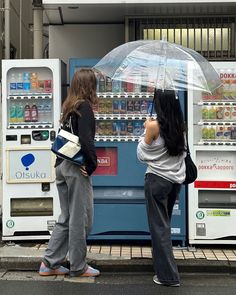 two women standing in front of a vending machine with an umbrella over their head