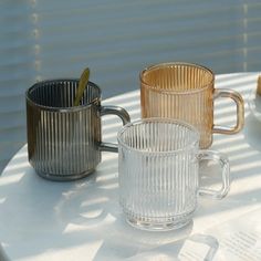 three glass mugs sitting on top of a table next to an empty plate and spoon