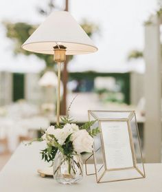 a table topped with a vase filled with white flowers and a framed photo next to a lamp