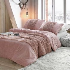 a bed with pink comforter and pillows in a room next to a window,