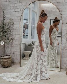 two women in wedding dresses looking at their reflection in a mirror while another woman stands nearby