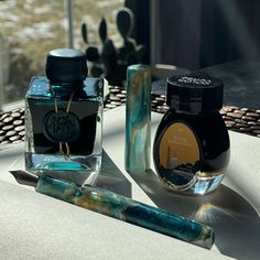 two bottles of ink sitting on top of a table next to a pen and paper