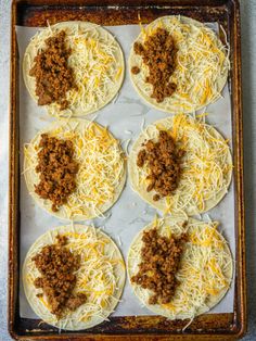 six tortillas with ground beef and cheese on top in a baking sheet ready to go into the oven