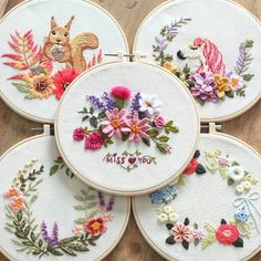 four embroidered hoops with flowers and animals on them sitting on top of a wooden table