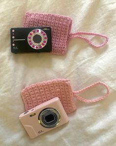 two knitted cameras and a camera case on a white bed with a pink strap