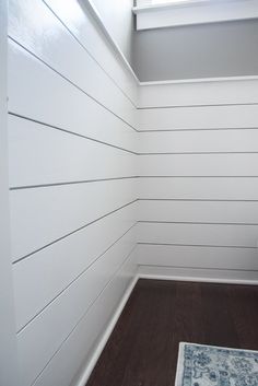 the corner of a room with white walls and wood flooring, along with a blue rug