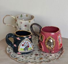 two coffee mugs sitting on top of a table next to each other with designs