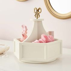 a white container with pink flowers in it on a table next to a gold mirror