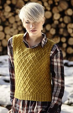 a woman standing in front of a pile of logs wearing a yellow sweater and plaid shirt